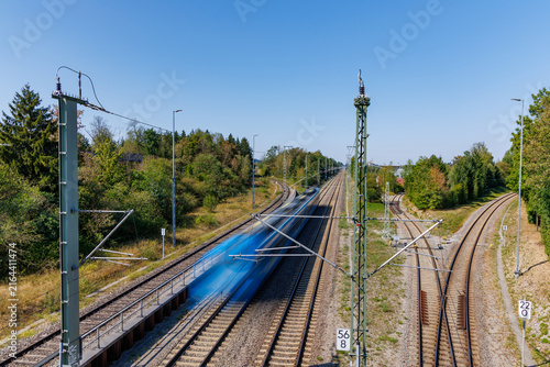 High angle view of motion blurred fast passenger train moving on railway tracks under blue sky, electric rail transport and speed concept