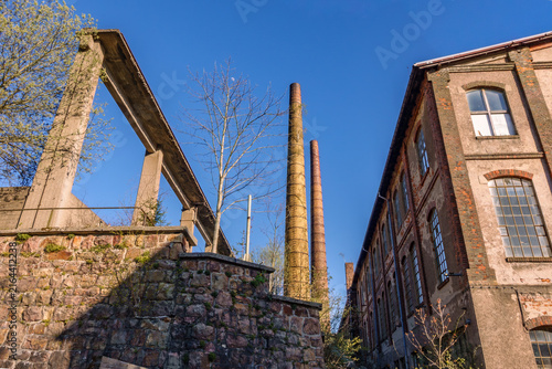 Old abandoned factory building with tall brick chimneys and concrete beam structure under clear blue sky, industrial heritage and lost places concept