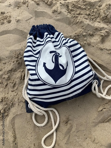Nautical Drawstring Backpack with Anchor Emblem Resting on Sandy Beach
