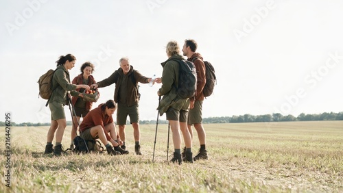 Hiking group taking a break on a field path and sharing fruit with each other