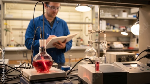 Scientist taking notes in a laboratory with red liquid in a glass flask on a hot plate
