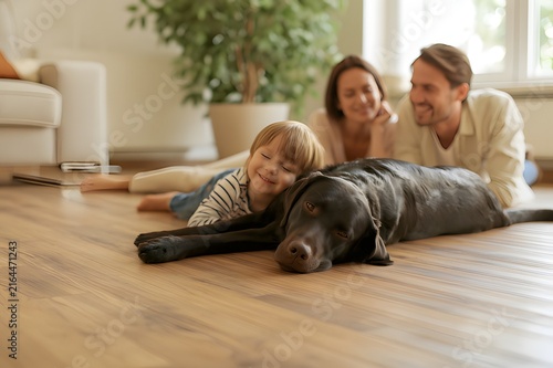 A happy young family with a little child hugging a black labrador dog on the floor inside a new apartment