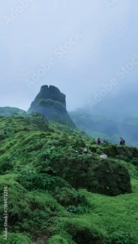 Canvastavla Hikers resting on ancient moss-covered stone ruins of a hill fort amidst heavy monsoon fog in the Western Ghats, India