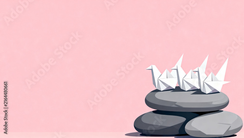 Minimalist still life composition with white origami paper cranes perched on stacked river stones against a soft pink background