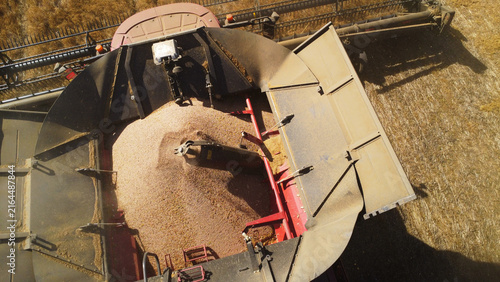 Foto A high-angle top-down aerial drone photograph offering a close-up perspective of a red combine harvester's grain hopper filling with freshly threshed grain
