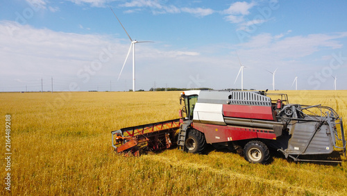 Fotografie Combine Harvester Operating in Field Near Wind Turbines