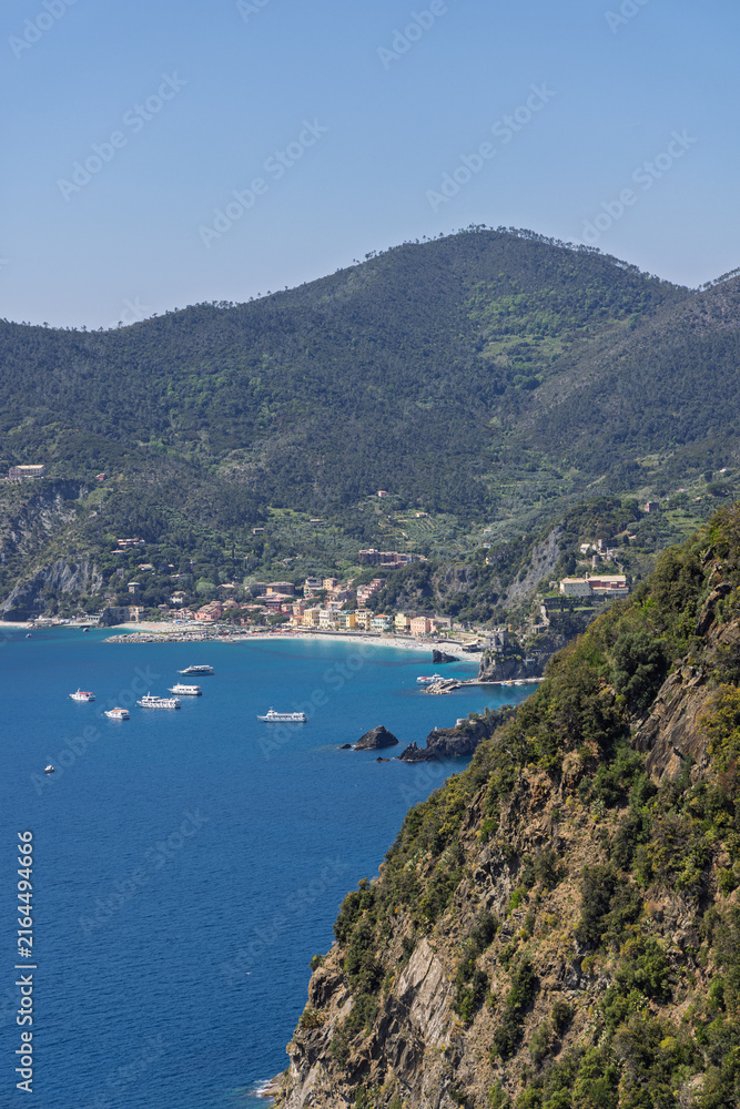 Fototapeta premium Passenger ferries at Monterosso al Mare, Italy show mountain and cliff scale around distant bay from high telephoto coastal perspective.