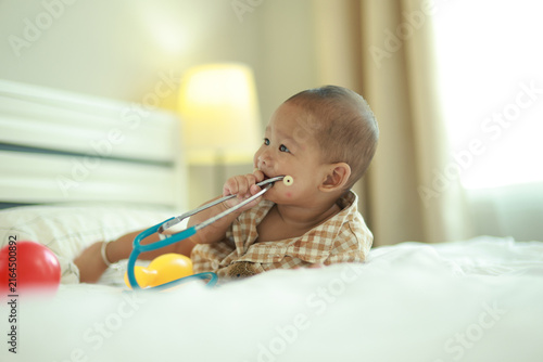 Принти на полотні Little boy, an Asian baby, crawls and plays on his bed at home his innocence and adorable cuteness making him look at a medical stethoscope as a fun toy