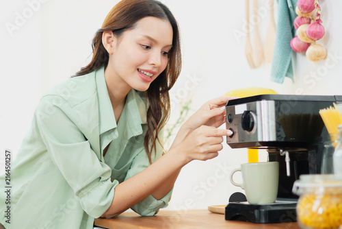 Obraz na płótnie Portrait beautiful Asian woman leaning against a wooden counter enjoying warm healthy coffee brewed modern coffee maker in her kitchen on a bright energetic and invigorating morning
