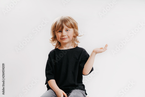 Cute little boy in black T-shirt is sitting on chair, smiling, and holding his hand near his face, showing that there's something on it.