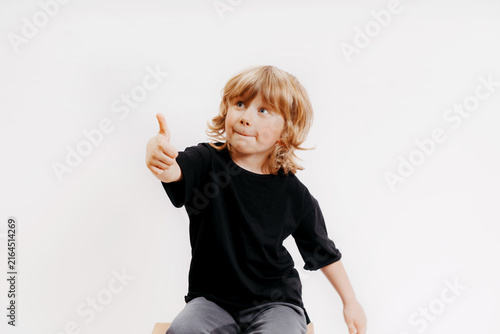 cute little blonde boy in black t-shirt is giving thumb up and smiling