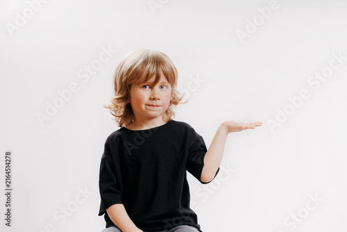 Cute little boy in black T-shirt is sitting on chair, smiling, and holding his hand near his face, showing that there's something on it.