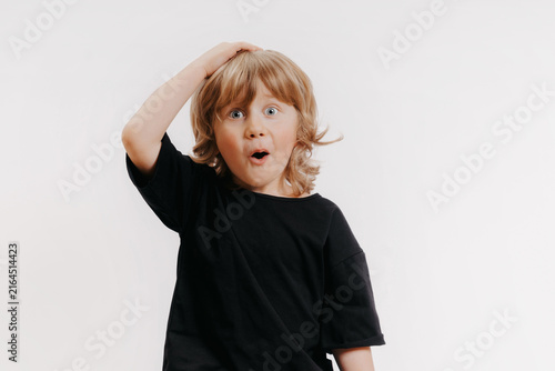 cute little blond boy in black T-shirt shows surprise and put his hand on his head