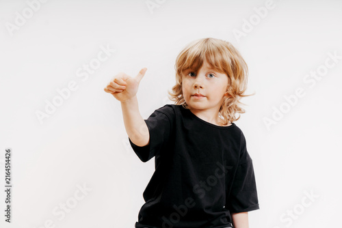 cute little blonde boy in black t-shirt is giving thumb up and smiling