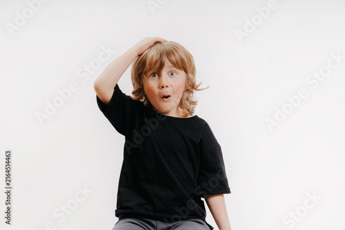 cute little blond boy in black T-shirt shows surprise and put his hand on his head