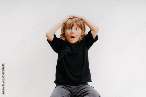 cute little blond boy in black T-shirt shows surprise and put his hand on his head