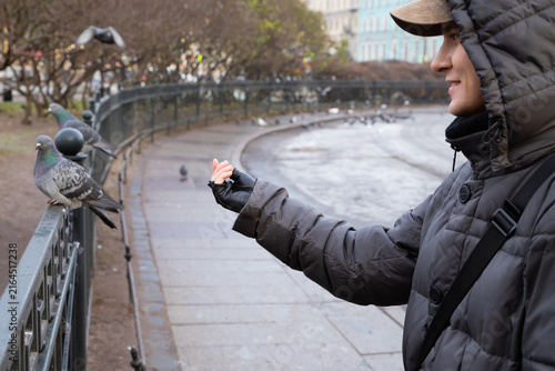 Young man feeding pigeon on city fence in autumn park. Human bird interaction and kindness to wildlife. Urban nature and compassion concept for lifestyle design and leisure activity