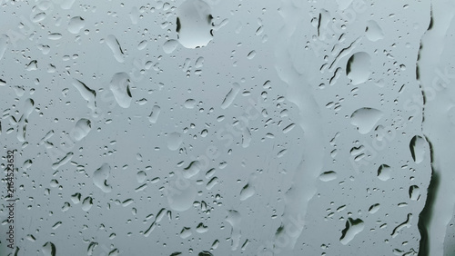 Fotografie Abstract wet glass window covered with rain droplets on gray background
