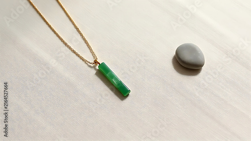 Slender green jade pendant on linen with river stone, natural wellness and jewelry concept.