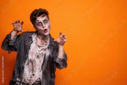 Scary zombie makeup and tattered clothes with outstretched hands on Halloween orange background with copy space