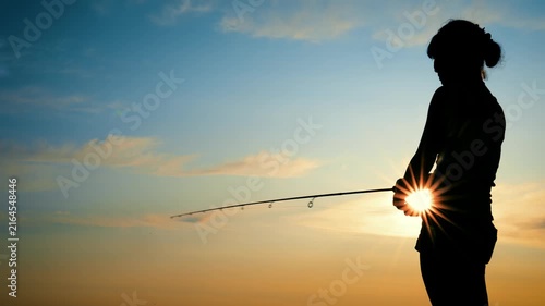 Silhouette of a woman holding a fishing rod against a sunset sky
