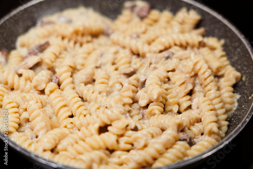 Fusilli pasta cooking in creamy mushroom sauce in pan. Close up of creamy fusilli dish with mushroom sauce.