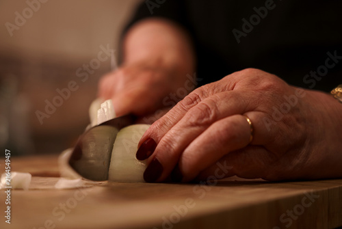Julienne cutting onion with knife on wooden cutting board. Woman chopping fresh onion with knife.