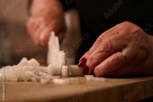 Dicing onion with knife on wooden cutting board close-up. Woman chopping fresh onion in dice with knife.