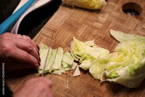 Shredding lettuce with knife into thin strips on cutting board. Woman cutting fresh lettuce with knife.