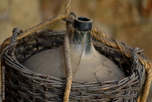 Foto Rare French antique wicker encased wine demijohn against a handcrafted stone wall