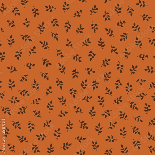 Seamless autumn botanical pattern with small dark brown leafy branches scattered on a burnt orange background. Warm minimal foliage design in earthy fall colors.