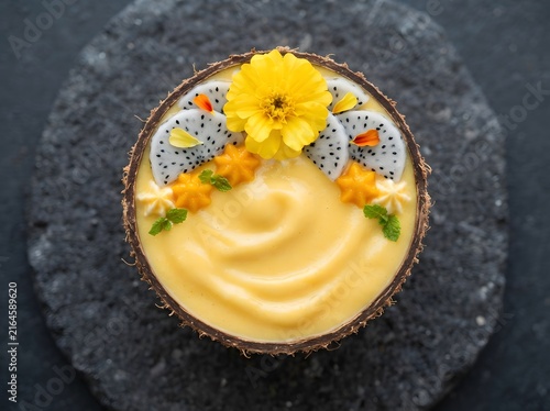 Tropical yellow smoothie bowl served inside a coconut shell with edible flower