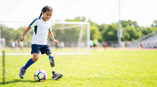 Girl with prosthetic leg playing soccer as adaptive youth sports and child amputee inclusion concept
