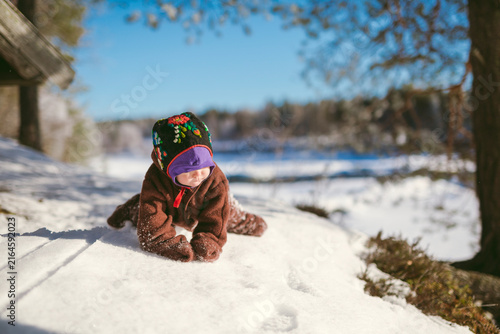 Toddler male in brown fleece suit crawling on snow