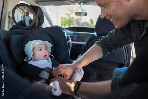 Father strapping his baby safely into black car seat