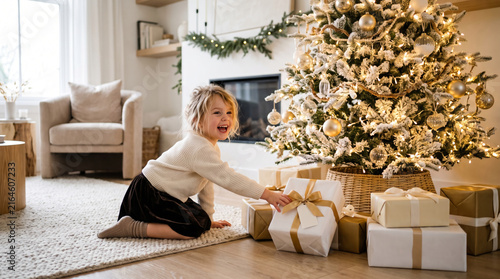 Joyful young girl reaching for Christmas presents under a decorated tree