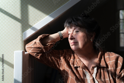 Sad mature woman leaning on bed while sitting lonely in bedroom at home