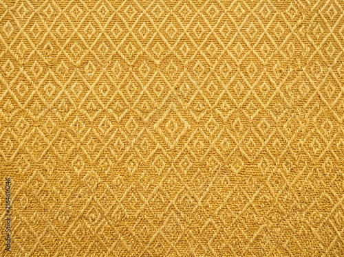 Textured golden yellow woven fabric featuring an intricate repeating geometric diamond pattern, ideal for upholstery or background design.