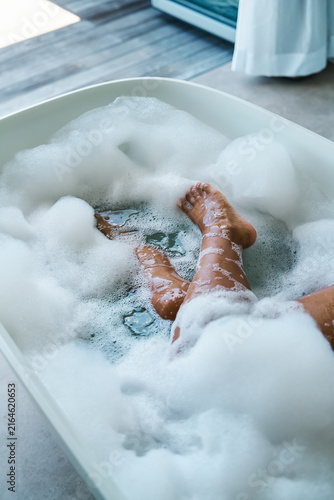 A white person relaxing in a bubble bath soaking legs and feet indoors