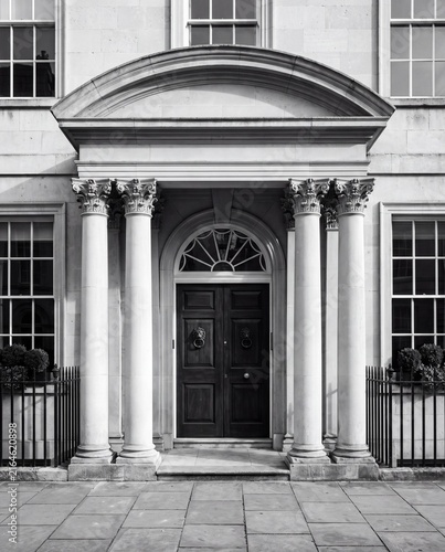 Symmetrical black and white view of a grand neoclassical building entrance featuring tall columns and a dark double door