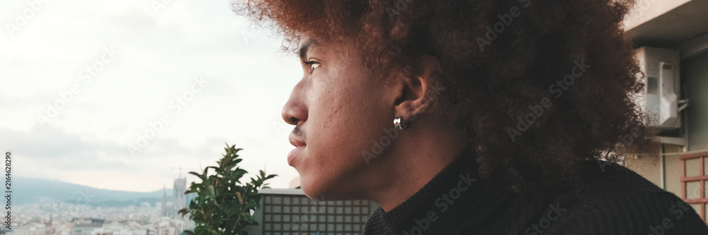 Fototapeta premium Close-up of young guy is standing on the balcony looking at the city . Panoramic