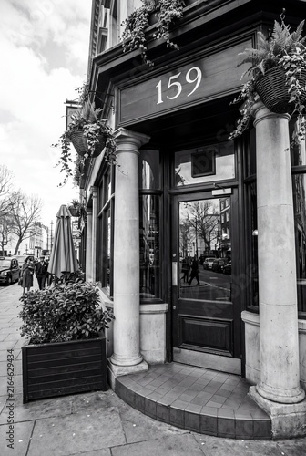 Black and white street view of a classic storefront entrance with stone columns and hanging plants