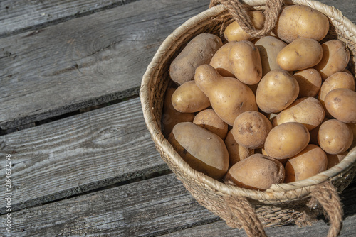 Fresh potatoes in a woven basket beside generous copy space on weathered wooden boards.