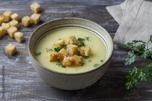 Creamy zucchini soup topped with golden croutons, fresh parsley and black pepper, served in a ceramic bowl on a dark rustic wooden table