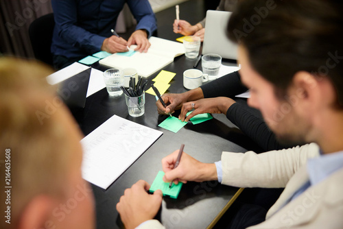 High angle view of business professionals writing ideas on adhesive notes in brainstorming session