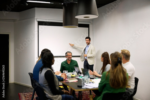 Businessman gesturing towards projection screen while talking his teammates