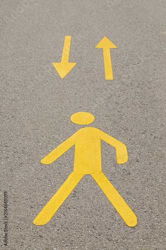 Yellow pedestrian icon and two way directional arrows on asphalt lane