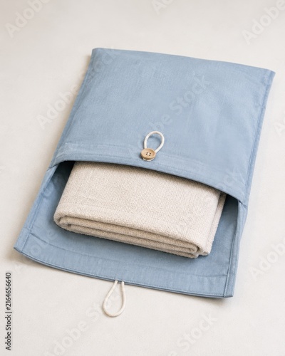 Blue fabric storage bag with button closure containing a rolled beige blanket, displayed on a light surface, showcasing a minimalist design and functional storage solution