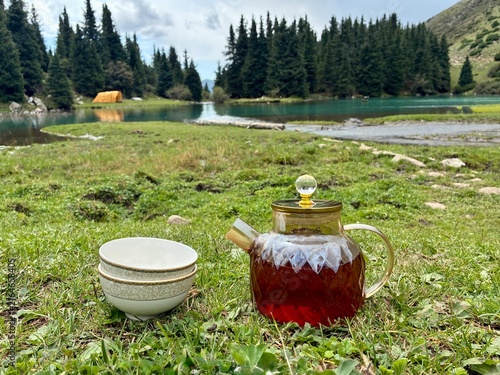 Quadro su tela Traditional Kyrgyz tea pot with two cups on the grass with beautiful lake backgr