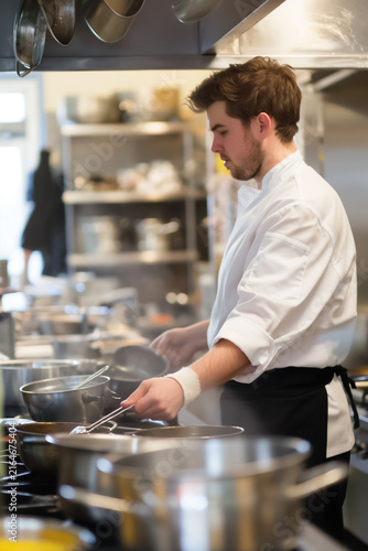 Professional chef cooking and stirring a pot in a busy restaurant kitchen
